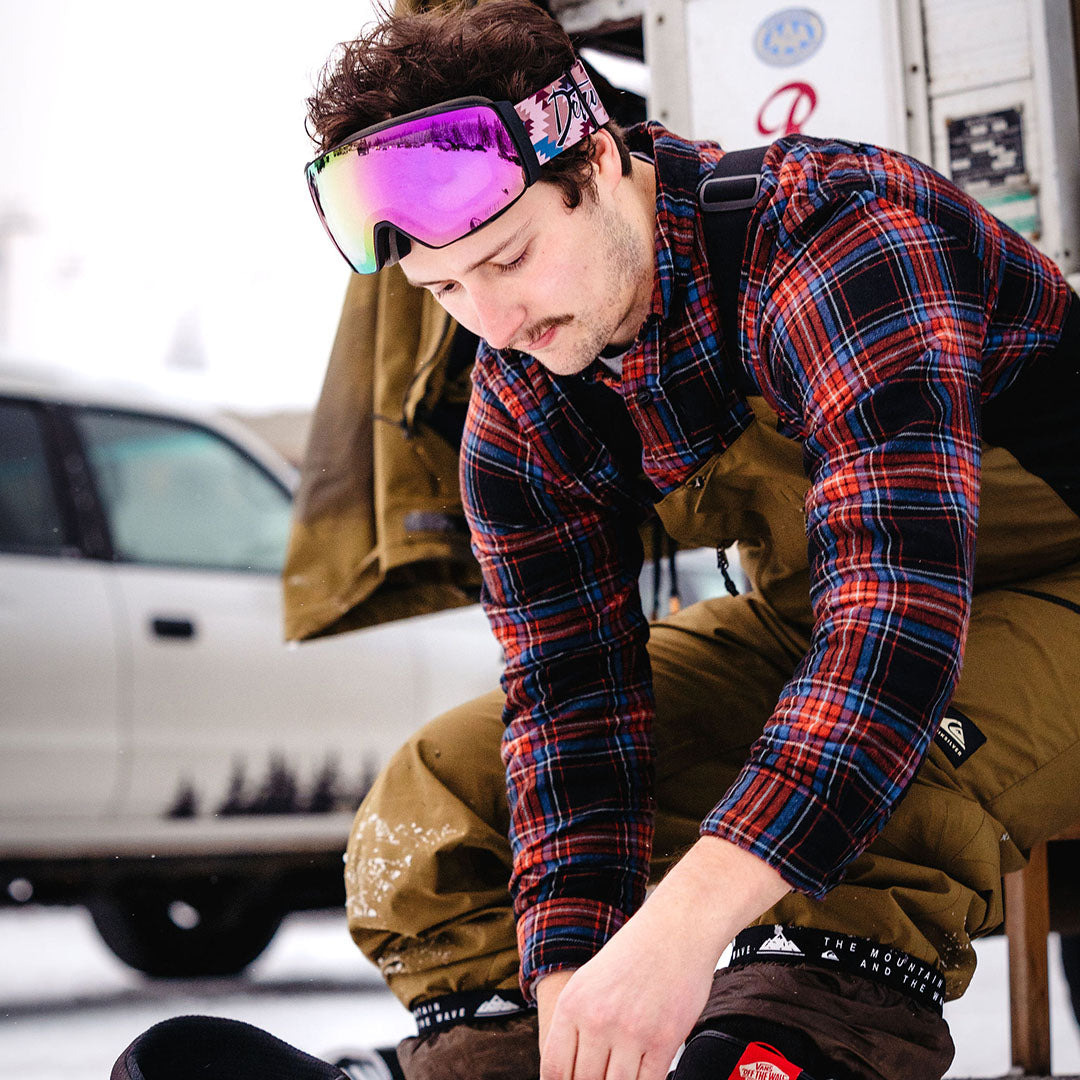 Person in ski gear, reflecting goggles, helmet, snowy landscape in background.